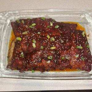 Glazed ribs topped with sesame seeds and sliced scallions in a glass baking dish.