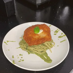 Breaded katsu cutlet on pesto pasta on a white plate